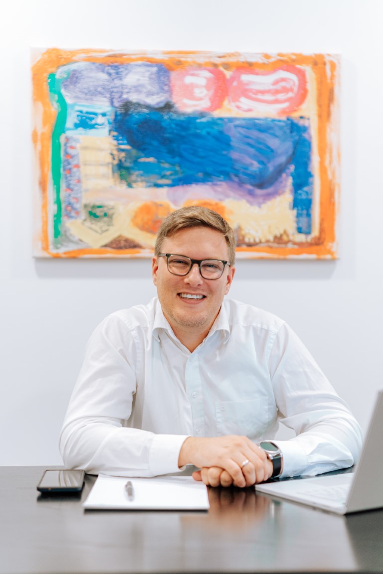 L&auml;chelnder Mann im B&uuml;ro vor buntem Gem&auml;lde