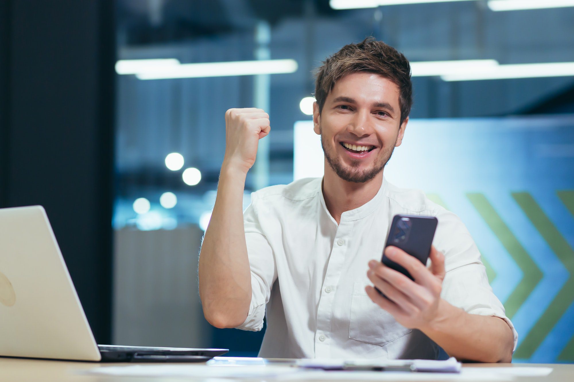 Portrait of a young businessman man smiles and rejoices in victory holds in his hands the phone